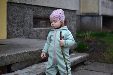 Naneli, yumuşak kabuklu bebek elinde ağaç dalı tutuyor ve baharda Doğu Avrupa 'daki apartman girişinin yanında yürüyor. Küçük kız dışarıda sopayla oynuyor..