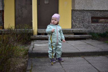 Naneli, yumuşak kabuklu bebek elinde ağaç dalı tutuyor ve baharda Doğu Avrupa 'daki apartman girişinin yanında yürüyor. Küçük kız dışarıda sopayla oynuyor..