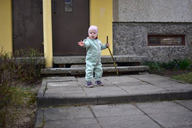 Naneli, yumuşak kabuklu bebek elinde ağaç dalı tutuyor ve baharda Doğu Avrupa 'daki apartman girişinin yanında yürüyor. Küçük kız dışarıda sopayla oynuyor..
