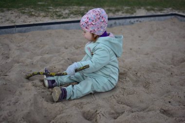 Küçük kız baharda kum havuzunda bir ağaç dalıyla oynuyor..