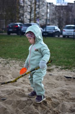 Küçük kız baharda bir arka bahçede kum havuzunda kürekle oynuyor..