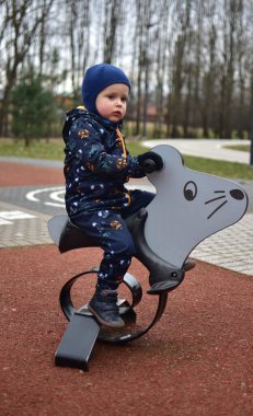 Küçük çocuk baharda çocuk parkında fare salıncağında oturuyor. Çocuk parkta sallanırken eğleniyor..