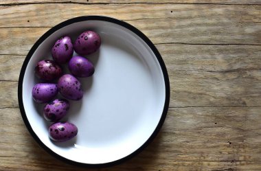 Ahşap bir masanın üzerinde mor bıldırcın yumurtaları olan bir kase. Menekşe desenli bıldırcın yumurtalarının kabuklu hali. Ahşap bir arka planda bir kase küçük noktalı yumurta. Kasede Paskalya yumurtası.