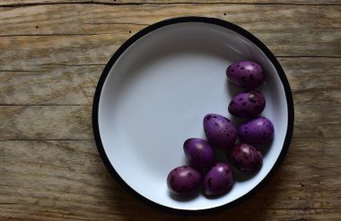 Ahşap bir masanın üzerinde mor bıldırcın yumurtaları olan bir kase. Menekşe desenli bıldırcın yumurtalarının kabuklu hali. Ahşap bir arka planda bir kase küçük noktalı yumurta. Kasede Paskalya yumurtası.