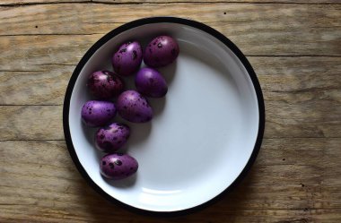 Ahşap bir masanın üzerinde mor bıldırcın yumurtaları olan bir kase. Menekşe desenli bıldırcın yumurtalarının kabuklu hali. Ahşap bir arka planda bir kase küçük noktalı yumurta. Kasede Paskalya yumurtası.