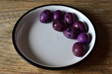 Ahşap bir masanın üzerinde mor bıldırcın yumurtaları olan bir kase. Menekşe desenli bıldırcın yumurtalarının kabuklu görüntüsü. Ahşap bir arka planda bir kase küçük noktalı yumurta. Kasede Paskalya yumurtası.