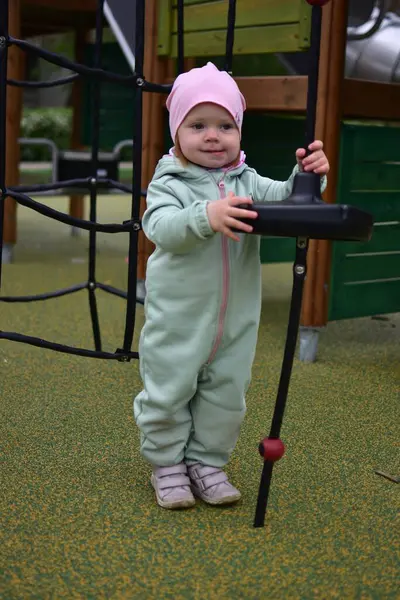 Yavru kız, soğuk baharda şehir parkındaki çocuk parkında ip tırmanışı yapıyor. Çocuk halk parkında ip ekipmanına tırmanmaya çalışıyor..