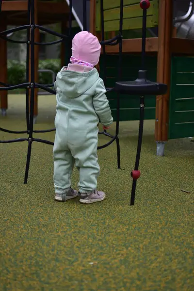 Yavru kız, baharda şehir parkındaki çocuk parkında tırmanma ağıyla oynuyor. Çocuk halk parkında ip ekipmanına tırmanmaya çalışıyor..