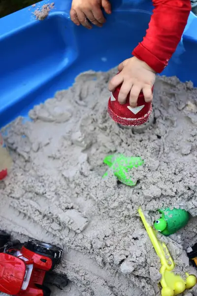 Küçük kız arka bahçede küçük bir kum havuzunda kum oyuncaklarıyla oynuyor. Yazın dışarıda eğlenen bir çocuk. Kumlu kum havuzu ve oyuncakları ayrıntılı görünümü kapat.