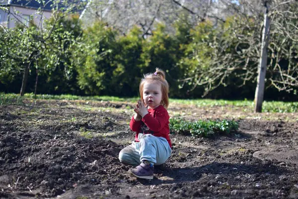 Yavru kız baharda arka bahçede toprakla oynuyor. Güneşli bir günde toprağın altında oynayan edepsiz görünümlü bir kız..