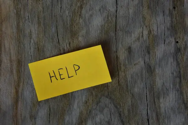 Tahta döşemeli arka plandaki sarı yapışkan nota mesaj yardımı. Mavi kalem kağıt üzerine kelime yardımı yazdı.