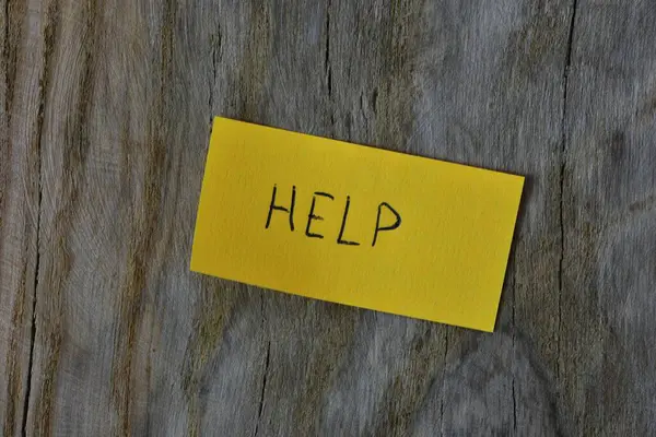 Tahta döşemeli arka plandaki sarı yapışkan nota mesaj yardımı. Mavi kalem kağıt üzerine kelime yardımı yazdı.