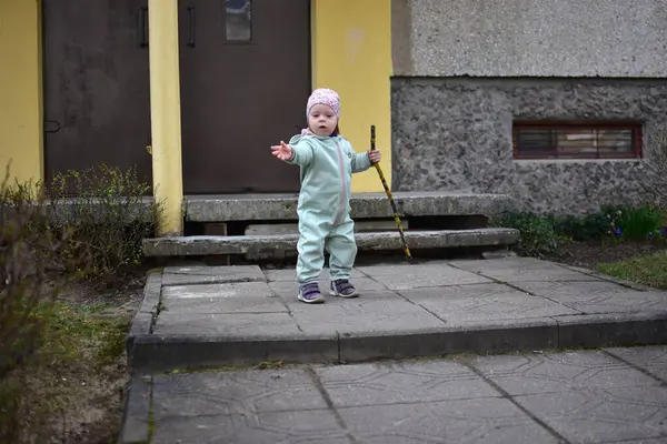 Naneli, yumuşak kabuklu bebek elinde ağaç dalı tutuyor ve baharda Doğu Avrupa 'daki apartman girişinin yanında yürüyor. Küçük kız dışarıda sopayla oynuyor..