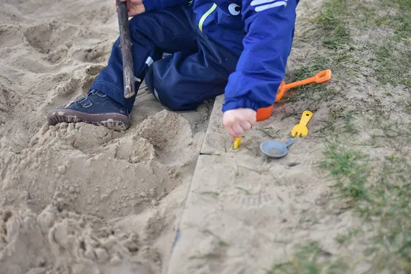 Küçük çocuk arka bahçedeki kum havuzunda bir kova ve kürekle oynuyor. Çocuk baharda dışarıda oyuncaklarla kum yemeği yapıyor..