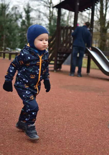 Küçük çocuk baharda çocuk parkında koşuyor. Babası da kızının aşağı kaymasına yardım ediyor. Çocuklar baharda parkta eğleniyor..