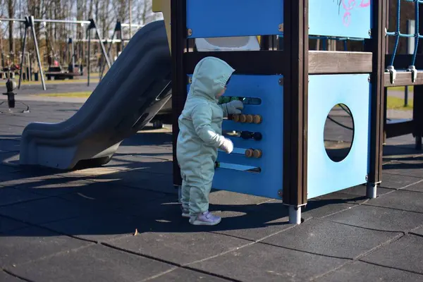 Yavru kız soğuk baharda şehir parkında çocuk parkında oynuyor. Küçük kız kış güneşli bir günde halk parkında eğleniyor..