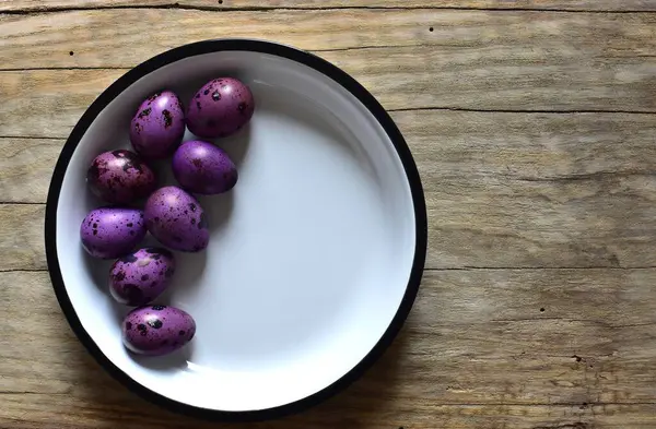 Ahşap bir masanın üzerinde mor bıldırcın yumurtaları olan bir kase. Menekşe desenli bıldırcın yumurtalarının kabuklu hali. Ahşap bir arka planda bir kase küçük noktalı yumurta. Kasede Paskalya yumurtası.