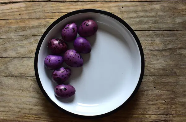 Ahşap bir masanın üzerinde mor bıldırcın yumurtaları olan bir kase. Menekşe desenli bıldırcın yumurtalarının kabuklu hali. Ahşap bir arka planda bir kase küçük noktalı yumurta. Kasede Paskalya yumurtası.