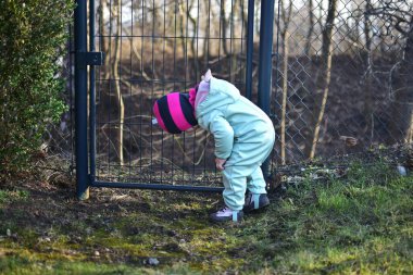 Metal tel çitlerin yanında duran küçük kız baharda zemini arıyor. İlkbaharda çitin yanında küçük bir kız..