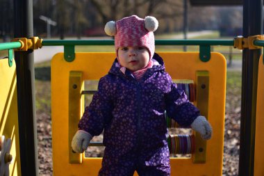 Yavru kız, baharda parktaki çocuk parkında gülümseyip oynuyor. Küçük kız kış güneşli bir günde halk parkında eğleniyor..