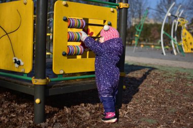 Yavru kız, baharda parktaki çocuk parkında gülümseyip oynuyor. Küçük kız kış güneşli bir günde halk parkında eğleniyor..