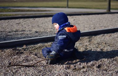 Küçük çocuk parkta güneşli bir sonbahar gününde ağaç dallarıyla, tahta çubuklarla oynuyor. Çocuk hayal gücünü kullanarak dışarıda eğleniyor..