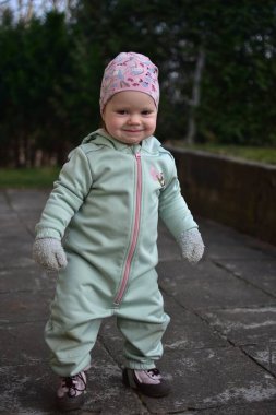 Nane kokulu, yumuşak kabuklu bebek baharda arka bahçede oynuyor. Gülümseyen küçük kız fayansların üzerinde yürüyor..