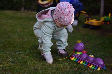 Naneli, yumuşak kabuklu bir beden giyen küçük kız baharda güneşli bir günde arka bahçede oyuncak kırkayakla oynuyor. Küçük kız dışarıda oyuncak bir böcekle yürüyor..