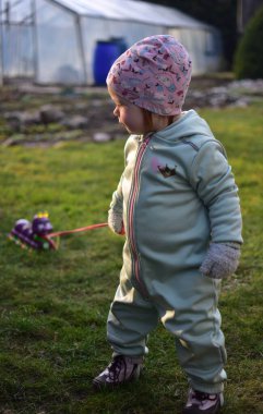 Naneli, yumuşak kabuklu bir beden giyen küçük kız baharda güneşli bir günde arka bahçede oyuncak kırkayakla oynuyor. Küçük kız dışarıda oyuncak bir böcekle yürüyor..