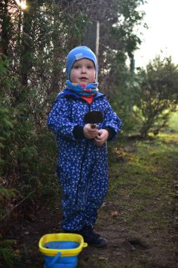 Mavi, yumuşak kabuklu mayolu çocuk baharda güneşli bir günde bahçedeki bir kovaya toprak kazıyor..