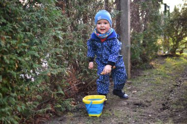 Mavi, yumuşak kabuklu mayolu çocuk baharda güneşli bir günde bahçedeki bir kovaya toprak kazıyor..