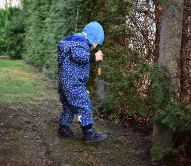 Mavi, yumuşak kabuklu mayolu çocuk baharda güneşli bir günde bahçedeki bir kovaya toprak kazıyor..