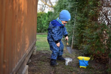 Mavi, yumuşak kabuklu mayolu çocuk baharda güneşli bir günde bahçedeki bir kovaya toprak kazıyor..