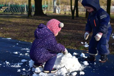 Küçük çocuk ve kız kardan adam yapmak için parkta oynuyorlar güneşli bahar zamanı. Erkek ve kız kardeş bahar zamanı son karla oynuyorlar..