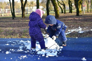 Küçük çocuk ve kız kardan adam yapmak için parkta oynuyorlar güneşli bahar zamanı. Erkek ve kız kardeş bahar zamanı son karla oynuyorlar..