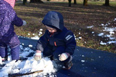 Küçük çocuk ve kız kardan adam yapmak için parkta oynuyorlar güneşli bahar zamanı. Erkek ve kız kardeş bahar zamanı son karla oynuyorlar..