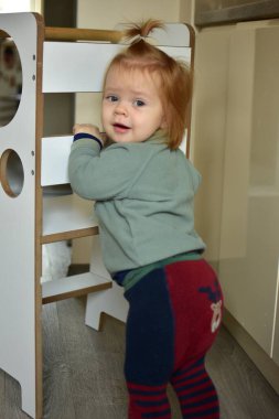 Kızıl saçlı at kuyruklu bebek. Kuleye yakın duruyor ve elleriyle tutuyor..