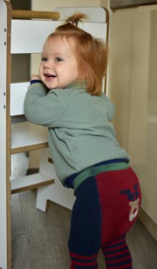 Kızıl saçlı at kuyruklu bebek gülümsüyor. Kuleye yakın duruyor ve elleriyle tutuyor..