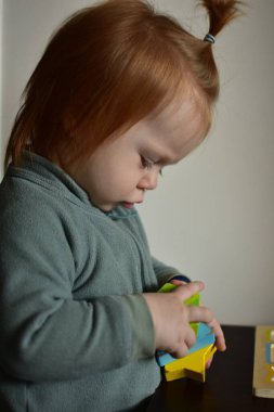 Kızıl saçlı at kuyruklu bebek elinde renkli bloklarla oynamaya odaklanmış..