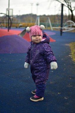 Yavru kız, baharda parktaki çocuk parkında gülümseyip oynuyor. Küçük kız kışın halk parkında eğleniyor..