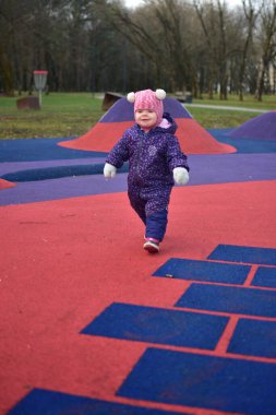 Yavru kız, baharda parktaki çocuk parkında gülümseyip oynuyor. Küçük kız kışın halk parkında eğleniyor..