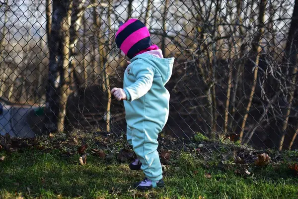 Baharda metal tel örgülerin yanında duran bebek profili. İlkbaharda çitin yanında küçük bir kız..