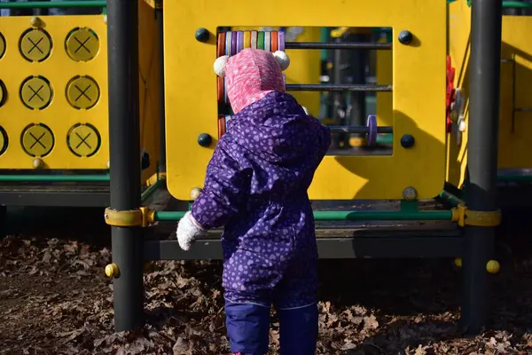Yavru kız soğuk baharda şehir parkında çocuk parkında oyun oynuyor. Küçük kız kış güneşli bir günde halk parkında eğleniyor..