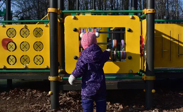 Yavru kız soğuk baharda şehir parkında çocuk parkında oyun oynuyor. Küçük kız kış güneşli bir günde halk parkında eğleniyor..