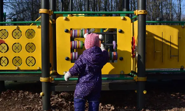 Yavru kız soğuk baharda şehir parkında çocuk parkında oyun oynuyor. Küçük kız kış güneşli bir günde halk parkında eğleniyor..