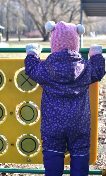 Yavru kız soğuk baharda şehir parkında çocuk parkında oyun oynuyor. Küçük kız kış güneşli bir günde halk parkında eğleniyor..