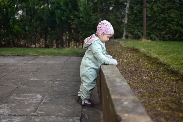 Nane kokulu, yumuşak kabuklu bebek baharda arka bahçede oynuyor. Küçük kız fayansların üzerinde yürüyor..