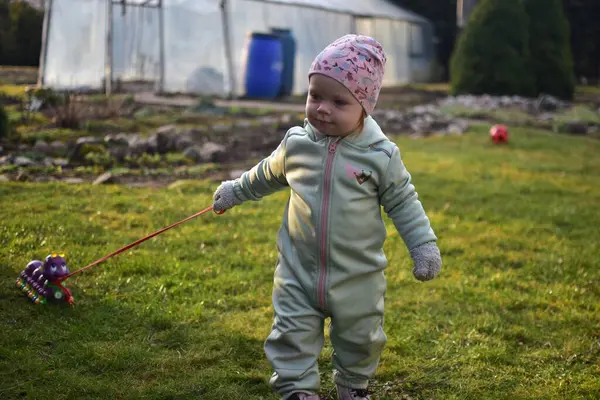 Naneli, yumuşak kabuklu bir beden giyen küçük kız baharda güneşli bir günde arka bahçede oyuncak kırkayakla oynuyor. Küçük kız dışarıda oyuncak bir böcekle yürüyor..