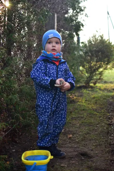Mavi, yumuşak kabuklu mayolu çocuk baharda güneşli bir günde bahçedeki bir kovaya toprak kazıyor..