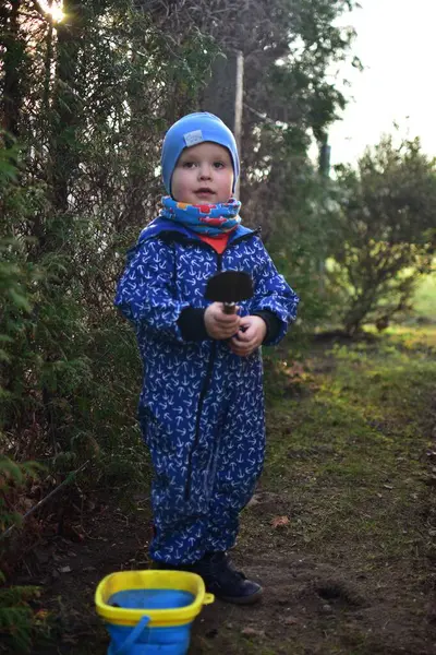 Mavi, yumuşak kabuklu mayolu çocuk baharda güneşli bir günde bahçedeki bir kovaya toprak kazıyor..